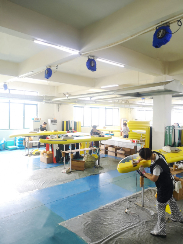 Skilled craftsmen hand-finishing inflatable paddle board seams in climate-controlled workshop